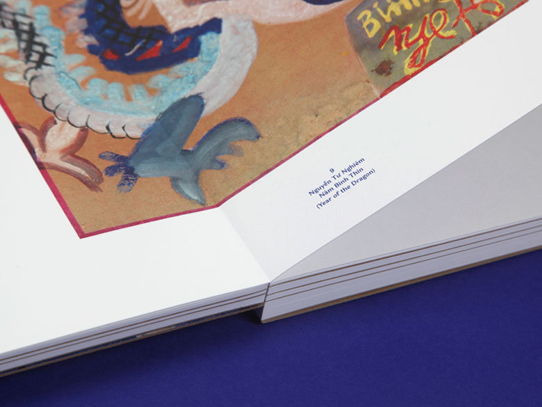 Open art book with sewn binding Open hardcover book with visible thread sewing along the spine, showing a colourful illustrated page and white endpapers on a blue surface.