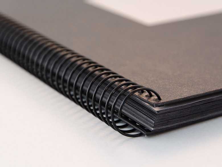 Black Wire-O Spiral Binding Close-up of a black wire-o bound booklet with black pages and a matte black cover.