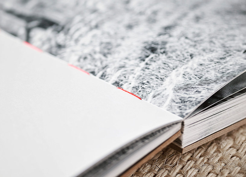 Offener Buchrücken mit Fadenheftung Nahaufnahme einer Fadenheftung in einem aufgeschlagenen Buch mit sichtbarem roten Bindefaden und offenen Buchblockkanten auf einem gewebten Untergrund.