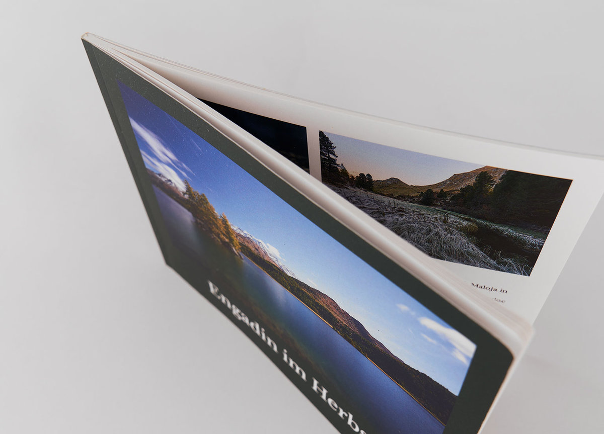 Brochure paysage ouvert avec images Brochure à couverture rigide avec une photo de paysage sur la couverture et plusieurs images de paysages visibles à l’intérieur, montrant un coin de la reliure.