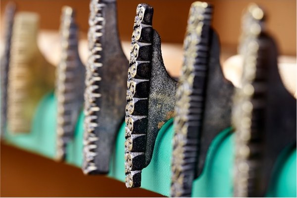Mehrere Buchbinderpressen mit gezackten Metallbacken, die ein grünes Band festhalten.