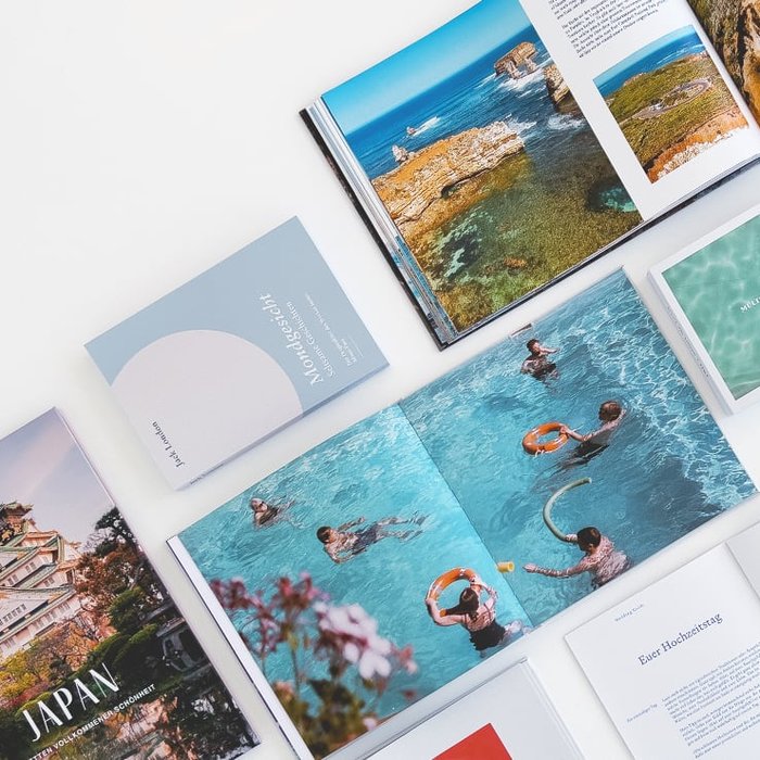 Mehrere geöffnete und geschlossene Bücher und Broschüren liegen ausgebreitet auf weissem Untergrund, darunter ein Buch mit dem Titel "Japan" und eine Broschüre mit Fotografien von Wasser- und Landschaftsszenen.