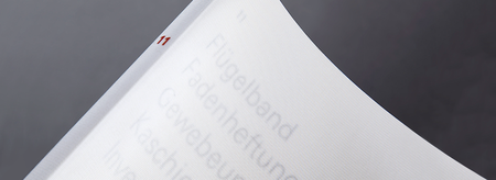 Weisser Buchrücken mit feiner Struktur, auf dem die Zahl 11 in Rot gedruckt ist, vorgelagert eine leicht transparente Seite mit aufgeprägten, schwach lesbaren Begriffen zu Bindetechniken.