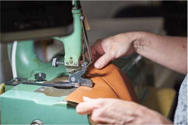 Hände führen eine orangefarbene Lederschicht unter die Nähmaschine zum Nähen.