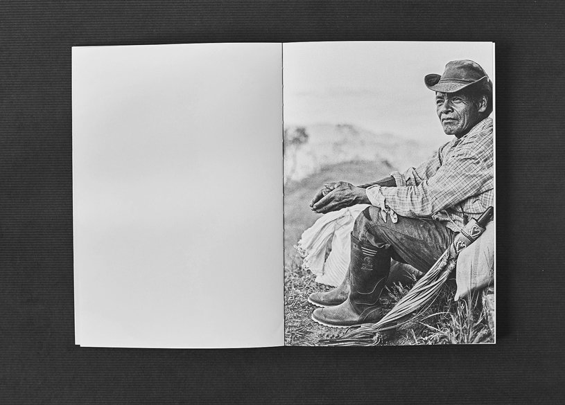 Buch mit Schwarz-Weiss-Fotografie auf rechter Seite Geöffnetes Buch mit einem schwarz-weiss Foto auf der rechten Seite, das einen Mann mit Hut und Stiefeln zeigt, der im Freien sitzt, die linke Seite ist leer.
