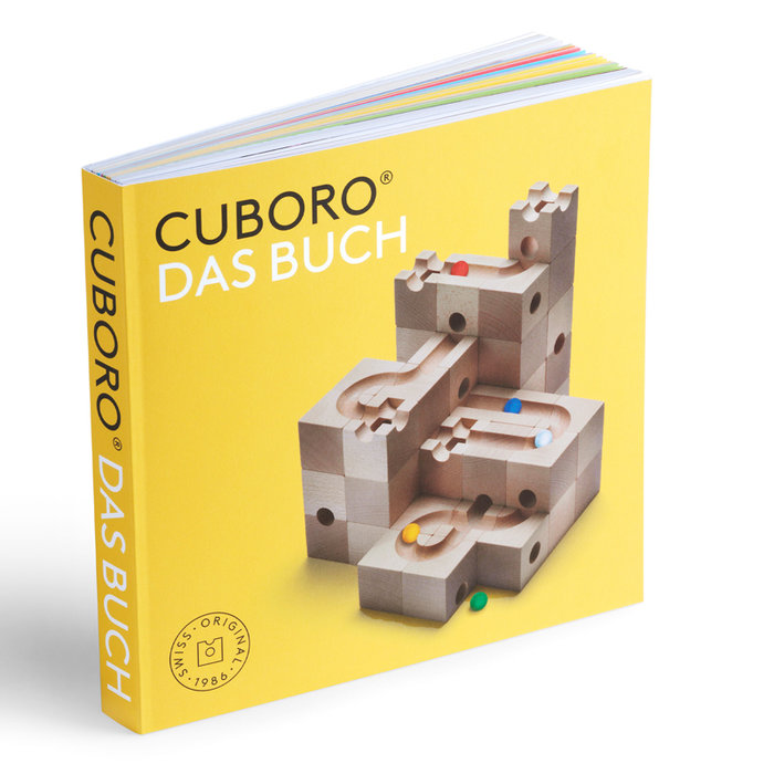 Quadratisches Hardcover-Buch mit gelbem Einband, Titel «CUBORO DAS BUCH» und einem Foto eines hölzernen Murmelbahn-Systems auf der Vorderseite.